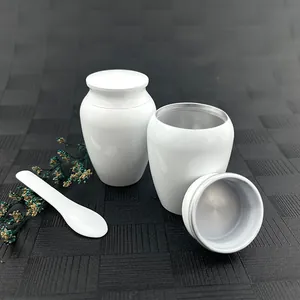 Detailed view of small white funeral urns showing open lid and matching white spoon