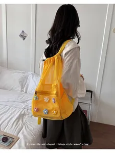Vista trasera de una mochila de malla amarilla con cordón y flores de colores aplicadas