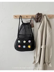Primer plano de una mochila de malla negra con cordón y flores tejidas de colores vivos