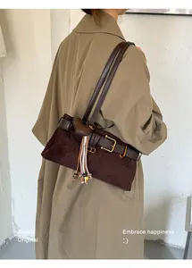 Detailansicht einer dunkelbraunen Wildledertasche mit Herzanhänger am Modell im Mantel