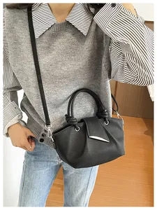 Dettaglio di una borsa a tracolla retrò nera a pieghe con un gilet in maglia grigio