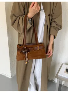 Detailansicht einer braunen Wildleder-Baguette-Tasche im Vintage-Stil mit Herzanhänger.
