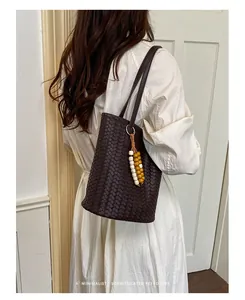 Nahaufnahme einer dunkelbraunen geflochtenen Eimertasche aus Leder zu einem weißen Kleid