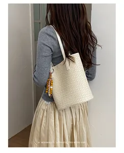 Elegant gestaltete, cremeweiße, gewebte Umhängetasche, an einem Model im Retro-Stil.