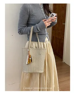 Detailansicht einer beige gewebten Tragetasche mit dekorativem Perlenanhänger.