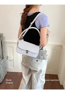 Back view of a model wearing a light grey nylon shoulder bag with buckle and card holder
