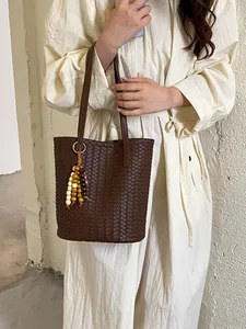 Elegante vintage braun gewebte Beuteltasche mit Holzperlen-Anhänger an einem Model