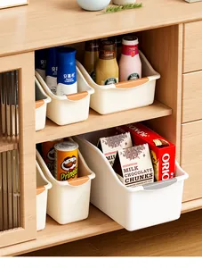 Detail view of white plastic storage bins organizing snacks in a wooden cabinet.