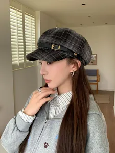 Detailed view of a retro grey plaid newsboy cap with leather buckle accent on a model