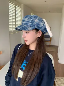 Close-up detail showing a blue plaid newsboy cap with plush bunny ears and bow