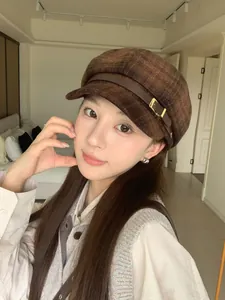 Detail view of a brown plaid newsboy hat worn by a model in a cozy indoor setting.
