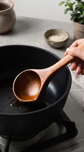 Detailed shot of a hand holding a 31cm long-handled wooden soup ladle over a black pot.