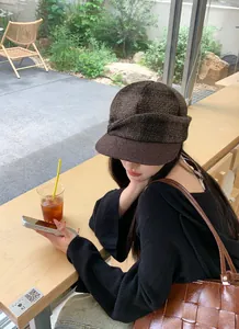 Woman wearing a vintage brown plaid woolen newsboy cap in a cozy outdoor cafe setting.
