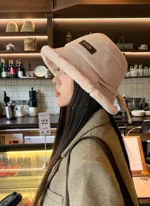 Side profile of a model wearing a fuzzy beige wool bucket hat in a cozy cafe setting.
