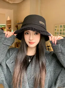 Close-up of a stylish black wool bucket hat with fur trim shown on a model in a cozy setting