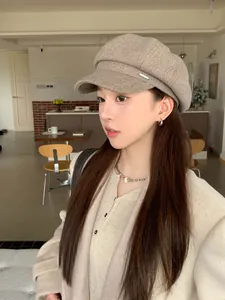 Close-up of a stylish khaki octagonal newsboy cap worn by a model in a cozy cafe setting.