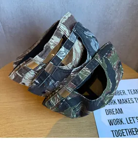 Vista dettagliata di cappellini camouflage a 5 pannelli impilati con fibbie regolabili.
