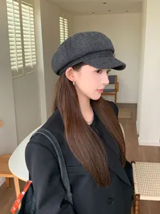 Side profile of a woman wearing a dark grey vintage newsboy cap in a bright room