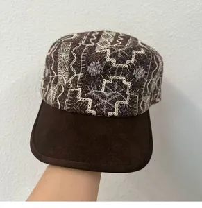 Close-up of vintage embroidered flat cap with white patterns and brown brim.