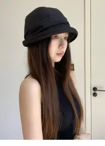 Side view of an Asian woman wearing a stylish black pleated bucket hat indoors.