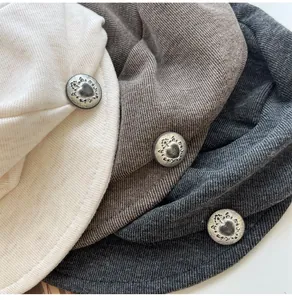 Close-up of pleated beret hats in neutral tones with vintage heart metal buttons