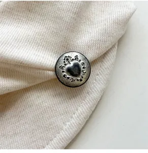 Close-up of beige knitted beret featuring a vintage silver heart-engraved button detail.