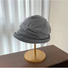 Detailed side view of a stylish gray pleated bucket hat on a display stand.