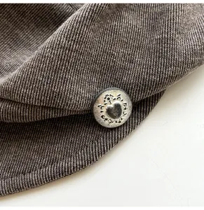 Close-up of vintage silver heart button on retro corduroy baker boy beret hat for women
