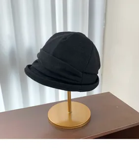 Detailed view of a black pleated bucket hat for women displayed on a golden stand