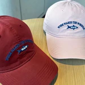 Close-up detail of small fish embroidery on pink and burgundy washed cotton baseball caps
