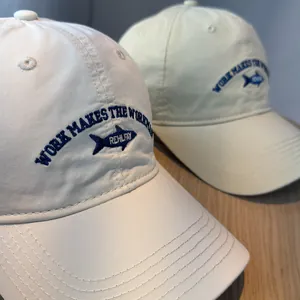 Detailed view of blue fish embroidery and slogan on a beige washed cotton baseball cap.
