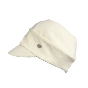 Close-up detail of the cream-white newsboy hat showing the fabric texture and metal tag.