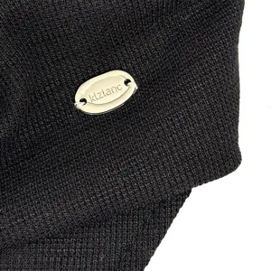 Macro detail of a black textured retro newsboy cap featuring a silver metal logo plate