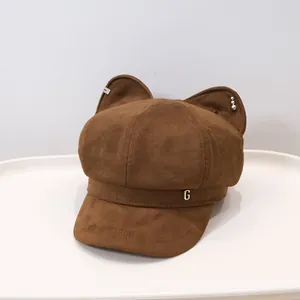 Detail of brown cat ear beret hat featuring metal letter G and pearl accents