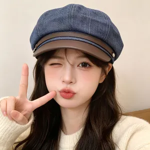 Asian model winking while wearing a blue denim newsboy hat with brown leather visor.
