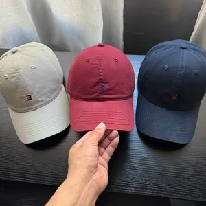 Hand hält eine kastanienbraune Baseballkappe neben marineblauen und beigen Hüten