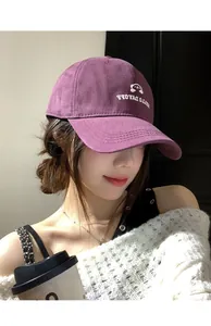 Detailaufnahme einer lila bestickten Baseballkappe, getragen von einem Model im Innenbereich