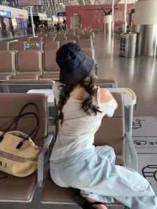 Vista trasera de una mujer con un elegante sombrero de pescador azul denim en el aeropuerto