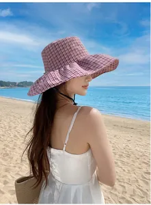 Woman wearing a pink plaid wide-brimmed sun hat on a sunny beach for sun protection