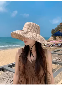 Close-up of a stylish woman wearing a plaid wide-brim sun hat at a scenic beach.