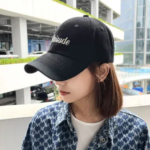 Detail view of a black baseball cap with white Attitude embroidery worn by a model