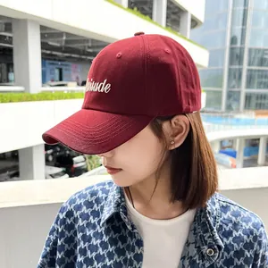 Detailed side view of a burgundy embroidered baseball cap worn by a stylish Asian model