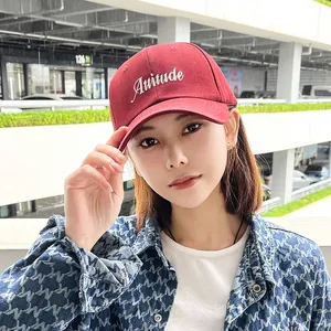 Close-up of burgundy baseball cap with Attitude embroidery worn by a stylish model