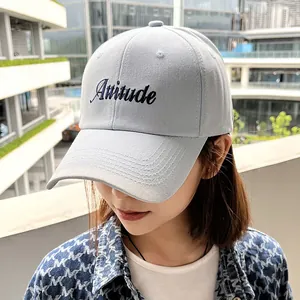 Detail view of light blue baseball cap featuring black Attitude embroidery on crown