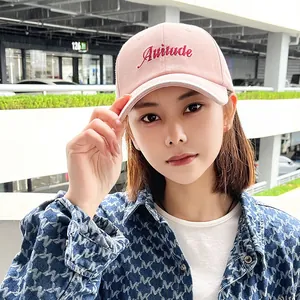 Close-up detail of a pink cotton baseball cap featuring Attitude embroidery worn by a model