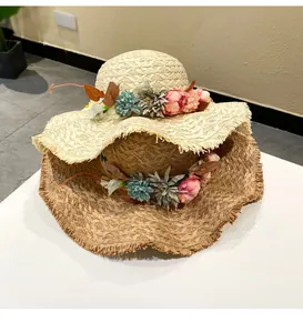 Detailed view of two hand-woven raffia straw sun hats with colorful flower wreaths.