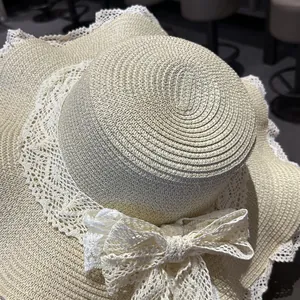 Dettaglio di un cappello di paglia beige con fiocco in pizzo e bordo a smerlo.