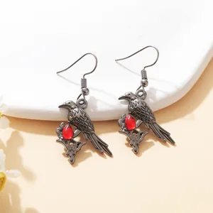 Close-up of gothic raven drop earrings with vibrant red teardrop gemstone accents.