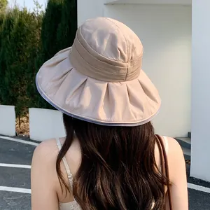 Back view of a stylish beige pleated sun hat for women shown in a sunny outdoor setting