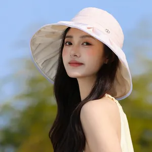 Elegant pink pleated sun hat for women featuring a stylish metal logo detail in sunlight.